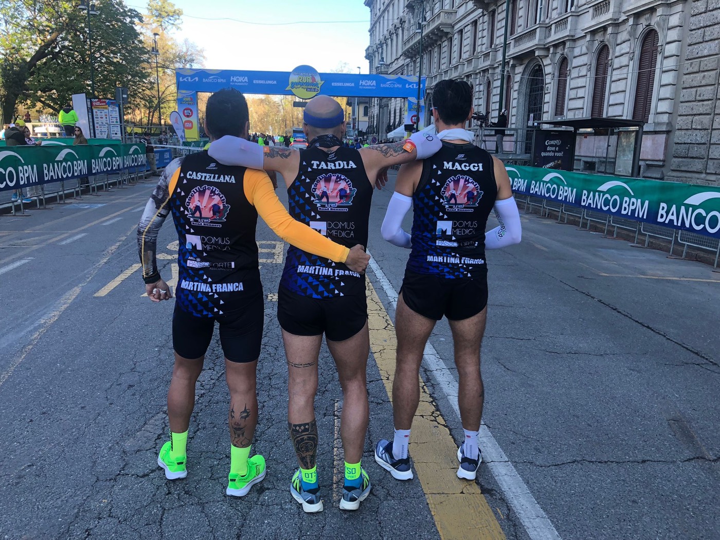 Tre atleti del team abbracciati sul percorso di gara, visti di spalle con la canotta ufficiale